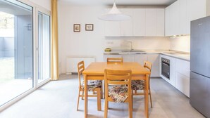 A modern kitchen with a dining table, chairs, a refrigerator, and a large window. - Bassani Garden (Bologna)