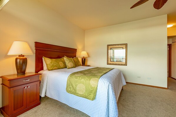A bedroom with a bed, two bedside lamps, a nightstand, a wooden headboard, a framed mirror, and a carpeted floor.