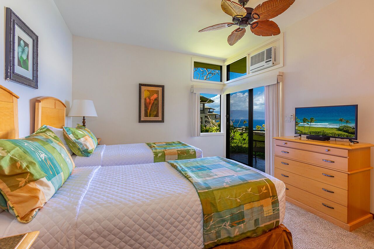 A hotel room with two beds, a ceiling fan, a TV, and a view of the ocean.