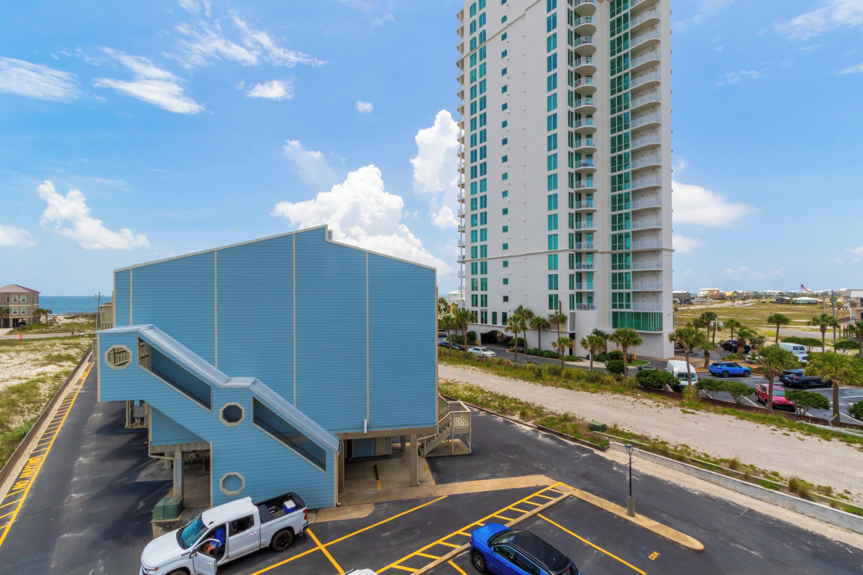 Un hotel con facciata blu, un parcheggio e un edificio alto sullo sfondo.
