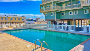 A swimming pool with a white fence and a multi-story building with balconies in the background. - Summer House West C201 (Gulf Shores)