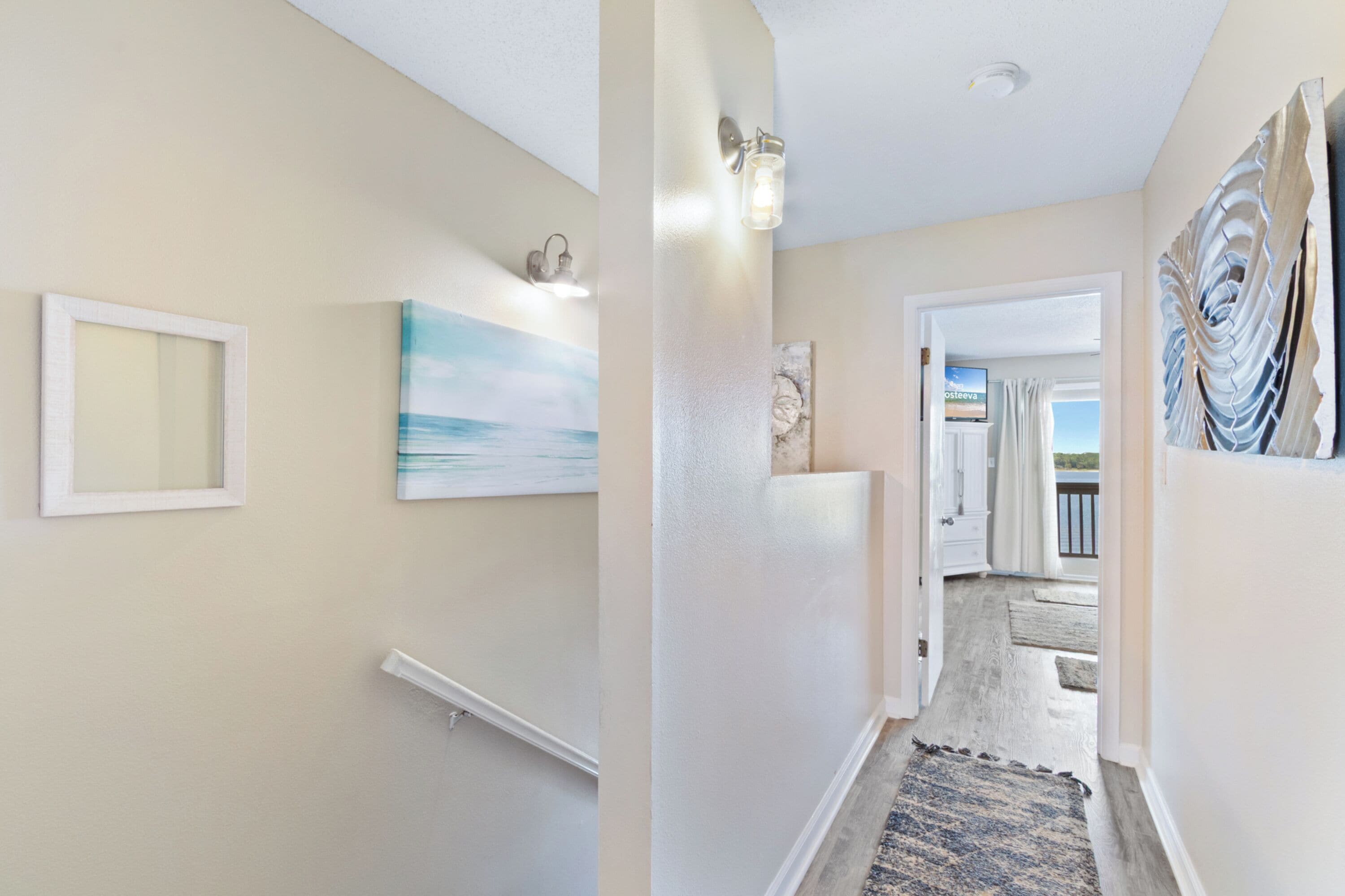A hallway with a light-colored wall, a framed picture, a painting, and a light fixture.