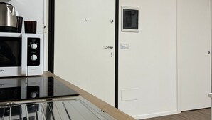 A modern kitchen with a microwave, kettle, and induction cooktop. There is a white door with a small window and a doorbell. - Savoy Apartment (Bari)