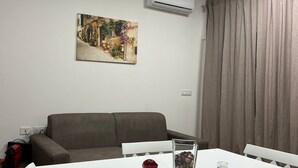 A modern living room with a white dining table, a brown sofa, and a painting on the wall. - Savoy Apartment (Bari)