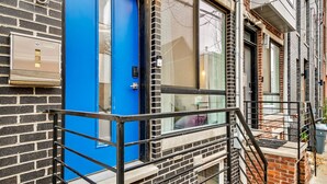 A building with a blue door, brick walls, and a metal railing.