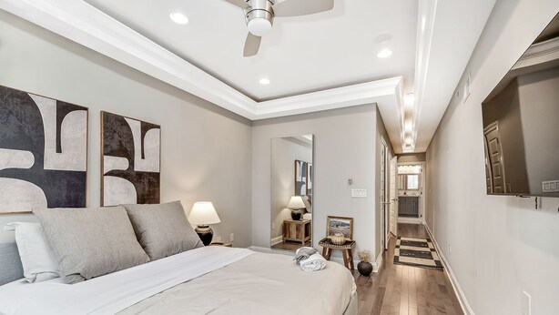 A modern bedroom with a large bed, bedside lamps, abstract wall art, and a hallway leading to a bathroom.