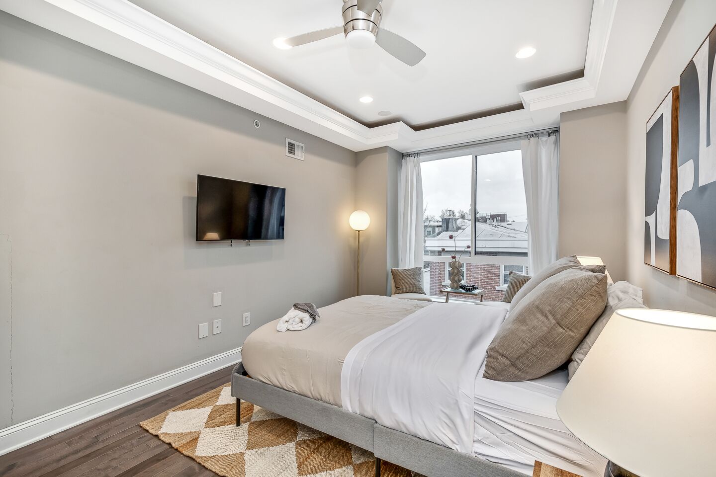 A modern bedroom with a bed, a TV mounted on the wall, a window with a view, and a ceiling fan.