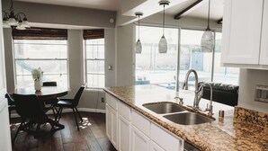 A kitchen with a granite countertop, white cabinets, a stainless steel sink, and pendant lights.