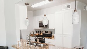 A modern kitchen with granite countertops, stainless steel appliances, and pendant lighting.