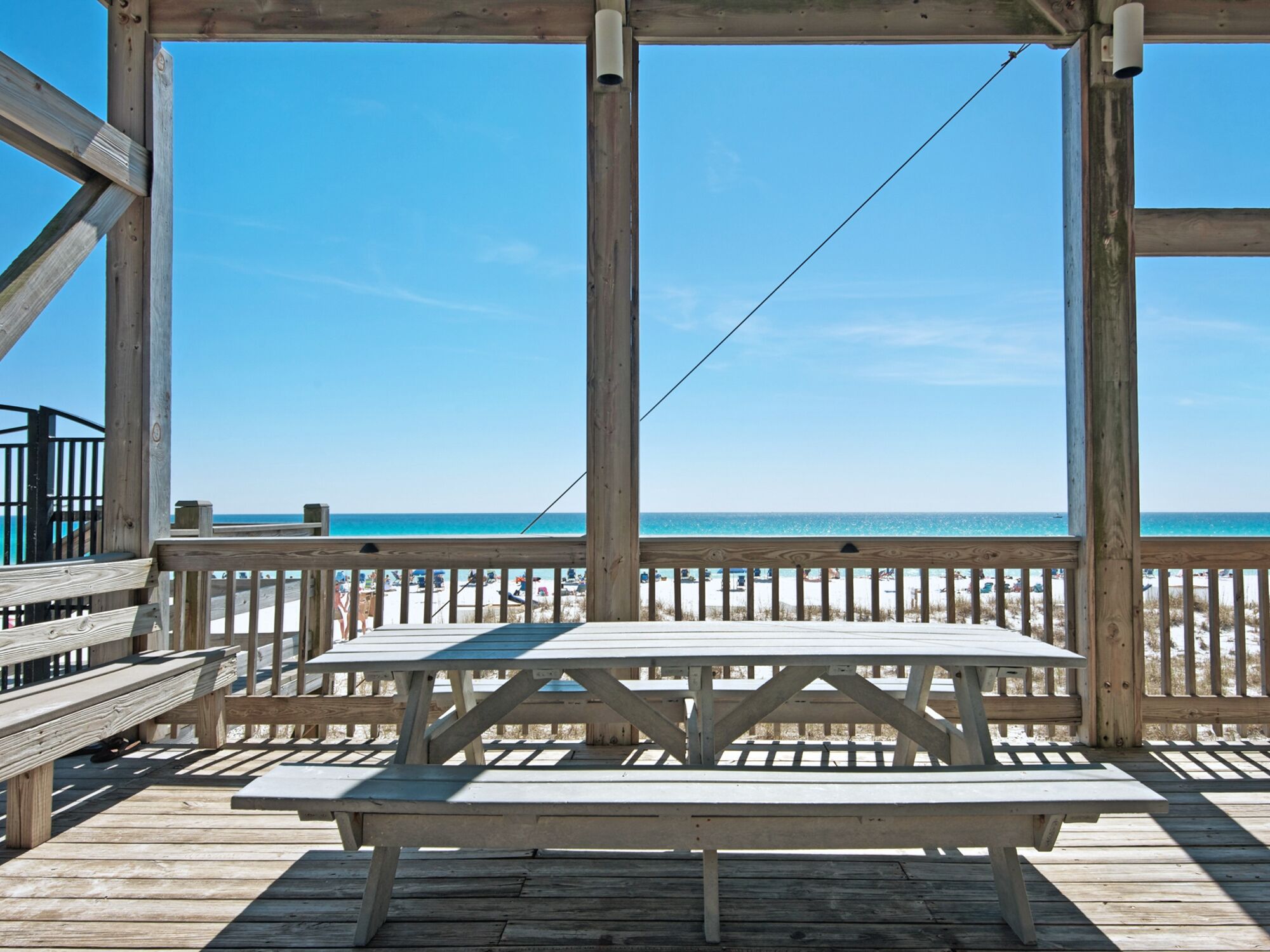 Una terraza de madera con una mesa de picnic y bancos que dan a una playa.