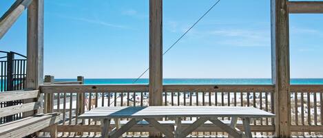 A wooden deck with a picnic table and benches overlooking a beach.