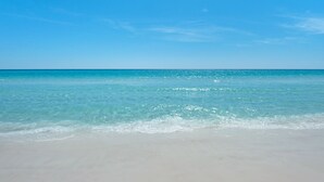 Ein Strand mit klarem türkisblauem Wasser und einem sandigen Ufer unter blauem Himmel.