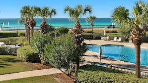 A pool area with palm trees, a view of the ocean, and a paved walkway. - Ground Floor Condo with Gorgeous Views (Miramar Beach)