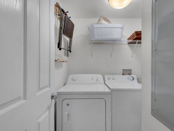 A laundry room with two white Whirlpool washers and dryers, a drying rack, and a basket on a shelf.