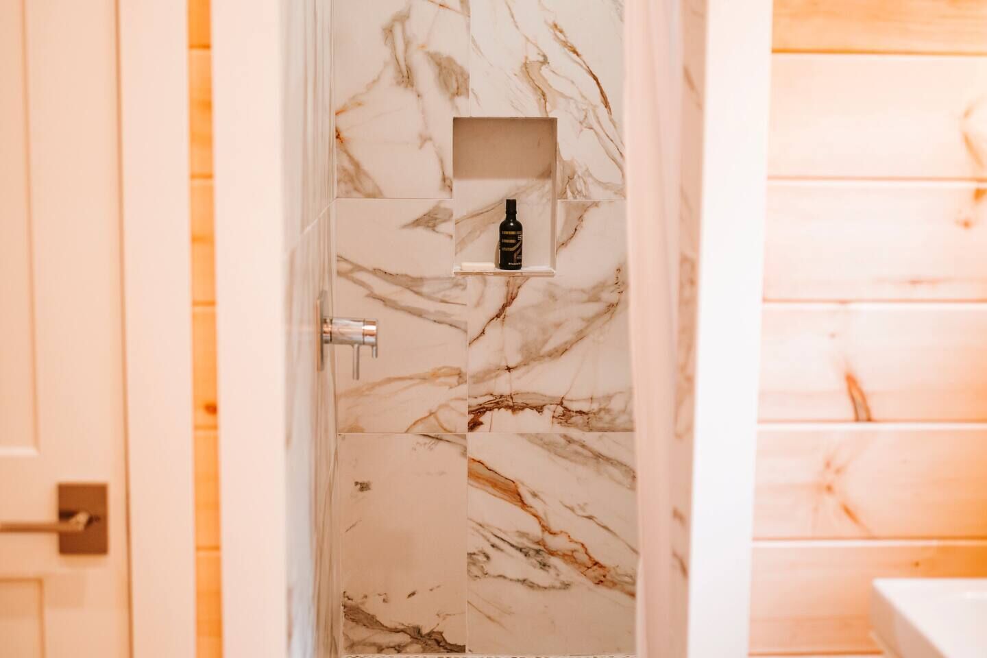 Een badkamer met een marmeren wand, een douchegedeelte en een plank met een fles.