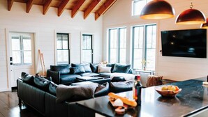 A modern living room with a black leather sofa, a large flat-screen TV, and a dining area with a marble countertop. - No Damage One of a Kind Stunning Lodge for 10 Walk Downtown Pool Hot tub  (Clayton)