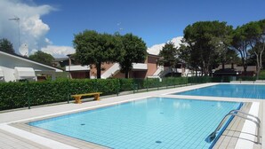 Ein rechteckiger Pool mit Fliesenbord und einer niedrigen Umzäunung, umgeben von Grünpflanzen.