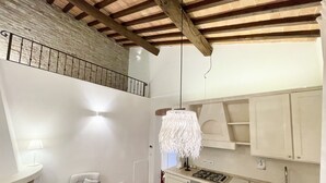 Une cuisine équipée d’une cuisinière à gaz, d’un four et de meubles blancs. On y trouve une chaise et une table sur laquelle est posé un panier.
