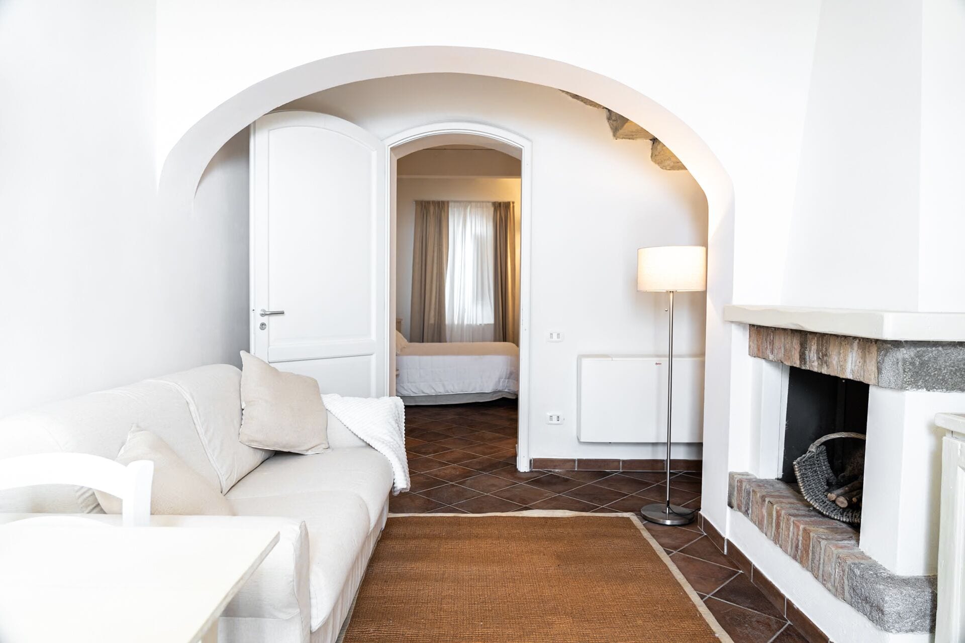 Un salon moderne avec un canapé blanc, une cheminée et un couloir menant à une chambre.