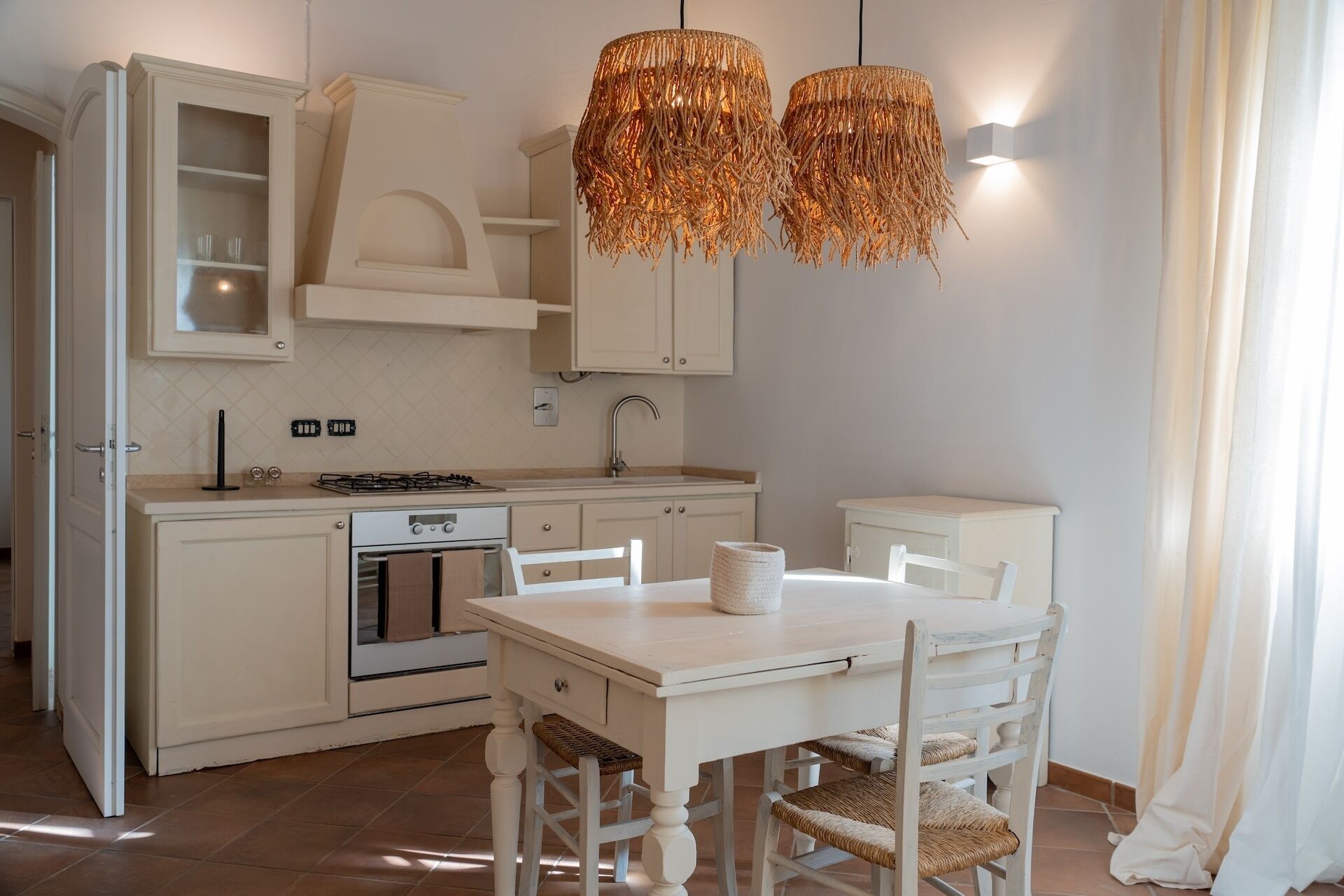 Una cocina con armarios blancos, una estufa y una mesa de comedor con sillas. Hay dos lámparas colgantes sobre la mesa.
