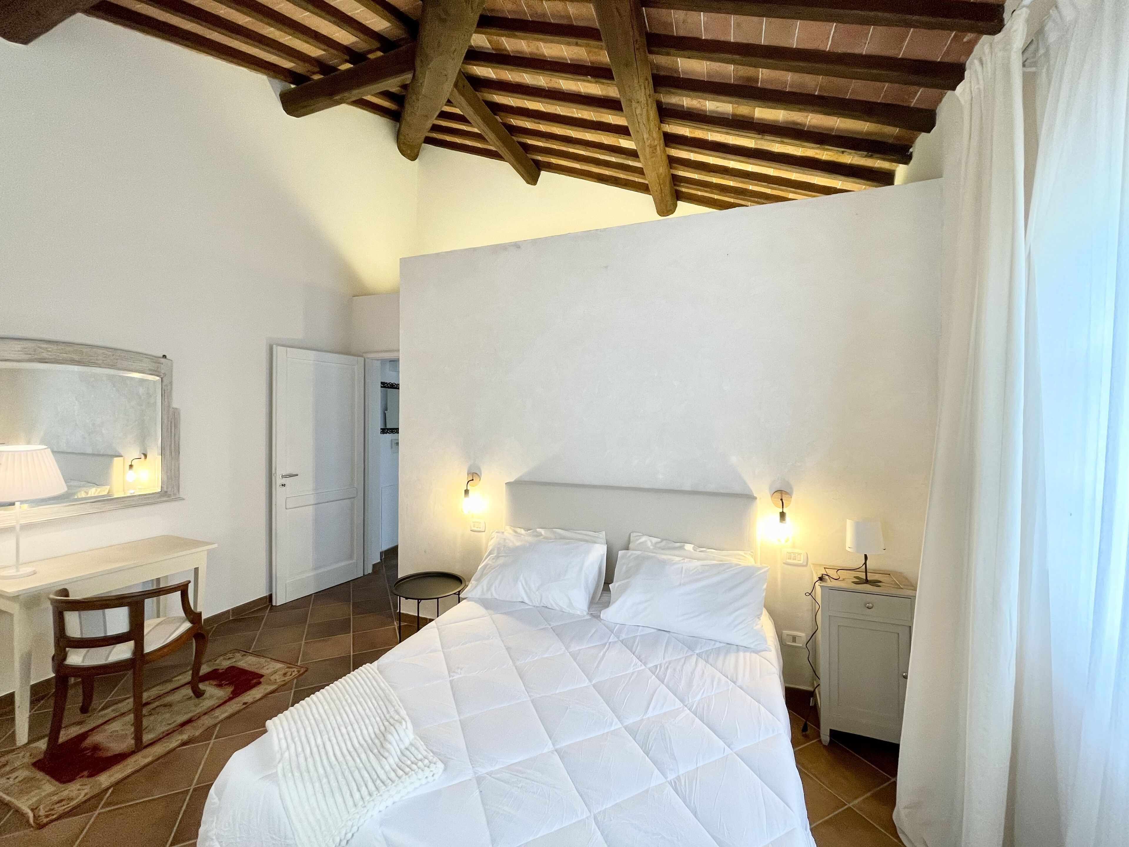 A bedroom with a bed, bedside tables, a mirror, and a desk.