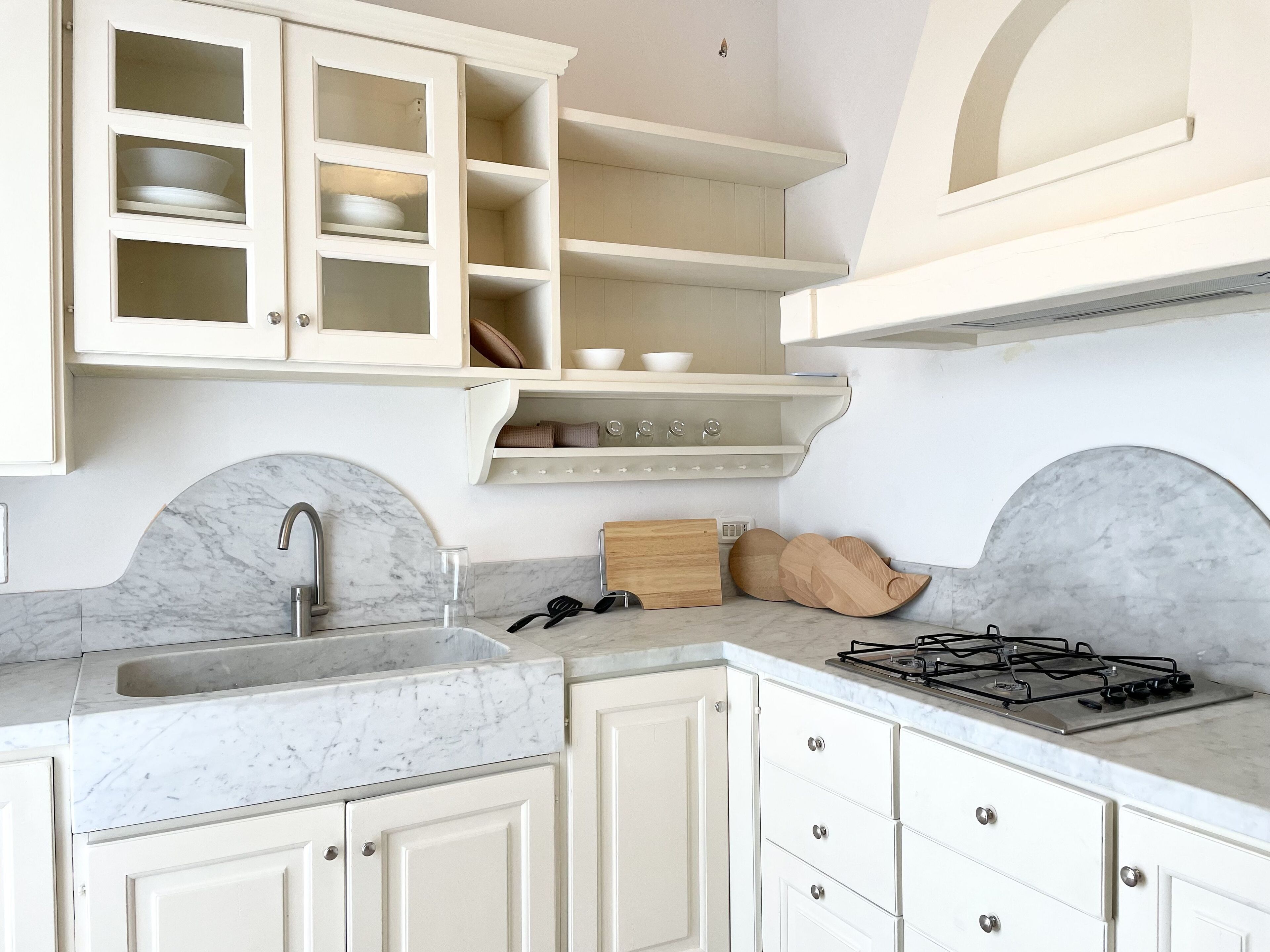 A kitchen with white cabinets, a marble countertop, a sink, a stove, and a shelf with dishes.