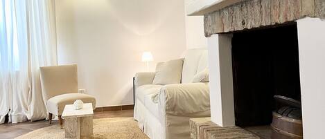 Una sala de estar con chimenea, un sofá, una silla, un tapete y una ventana con cortinas.
