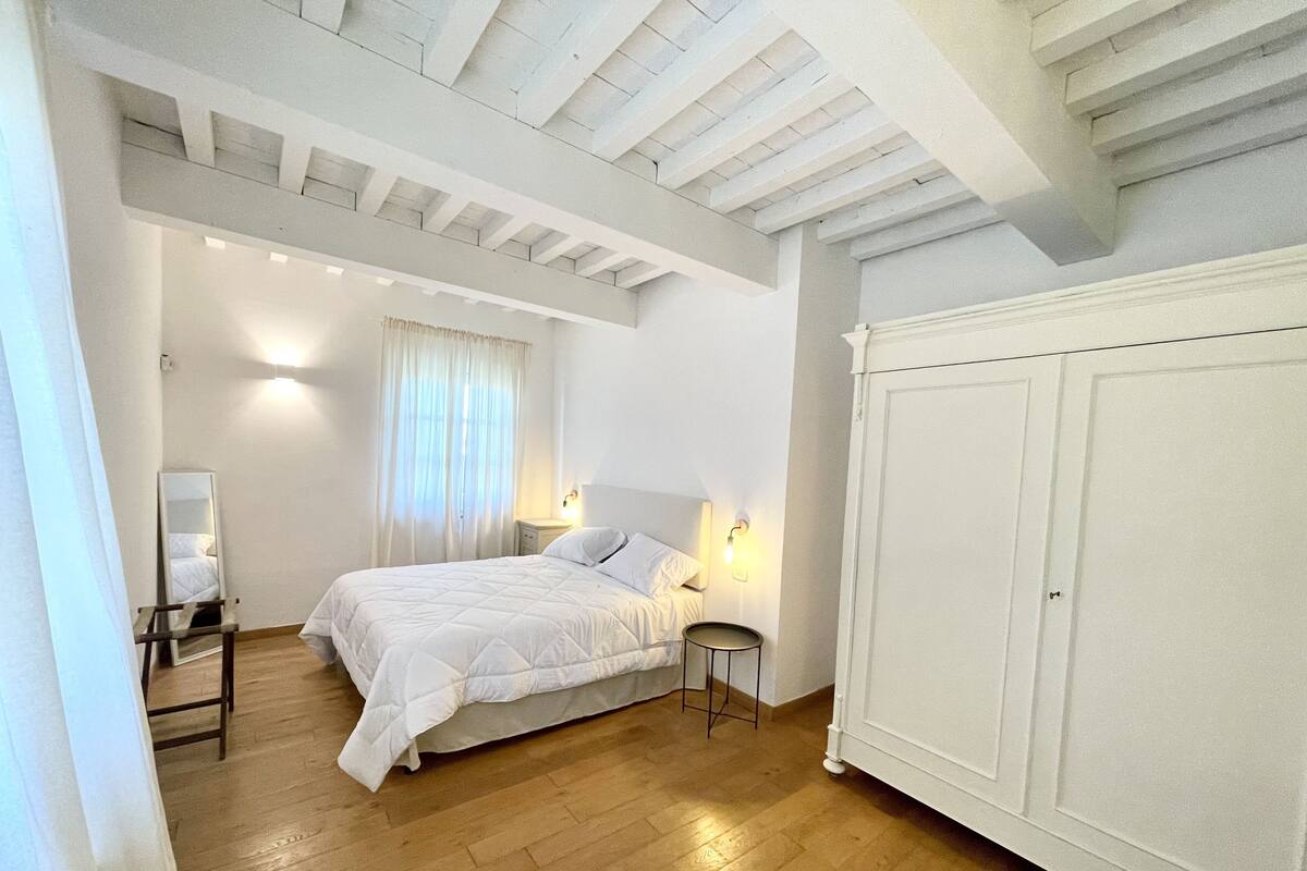 Un dormitorio con cama, mesitas de noche, armario y ventana con cortinas.