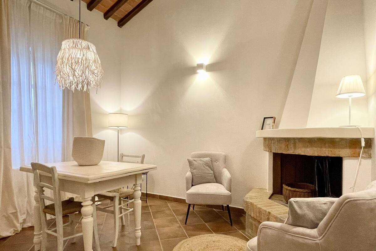 Una sala de estar acogedora con una mesa de comedor, dos sillas, una chimenea y una lámpara colgante.