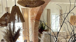 Une pièce avec une table en bois, un vase blanc contenant de l’herbe des pampas et des lampes suspendues en osier.