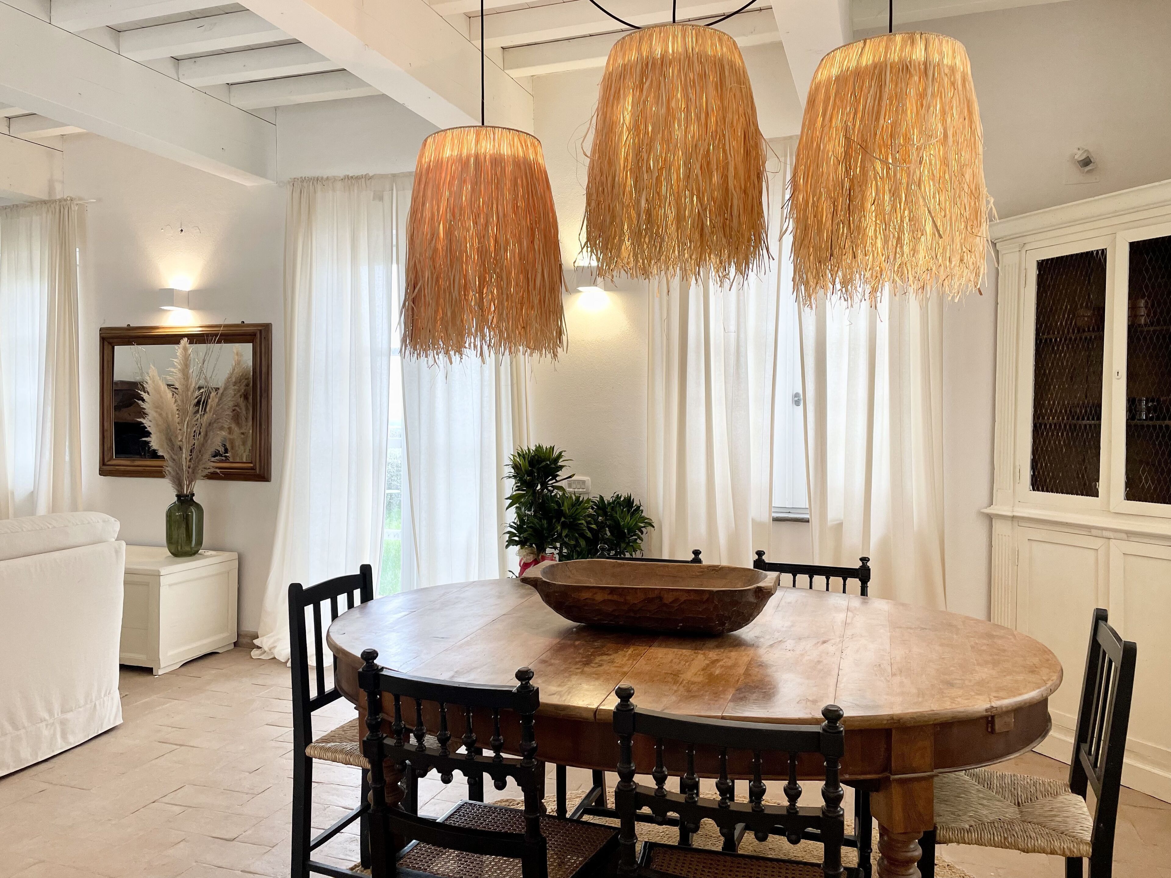 Un comedor con una mesa redonda de madera, sillas negras y tres lámparas de mimbre colgantes.