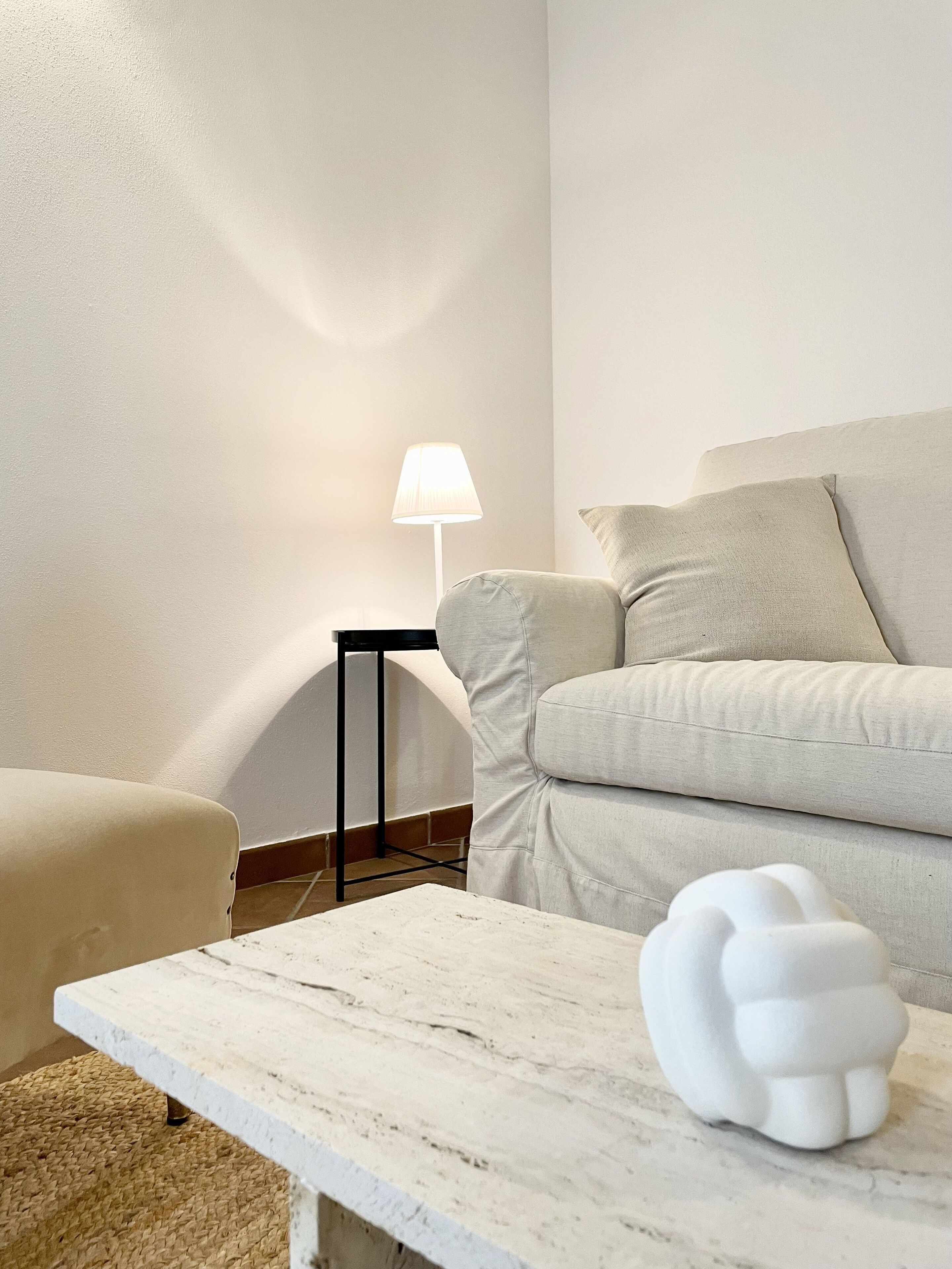 Uma sala de estar minimalista com um sofá branco, uma mesinha e um abajur.