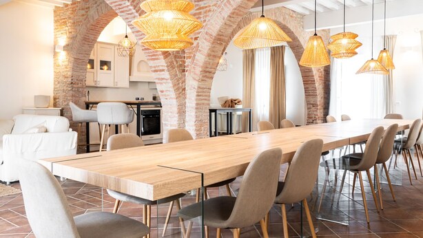 Un vaste espace dédié à la salle à manger, avec une longue table en bois, de nombreuses chaises et des lampes en osier suspendues au plafond.