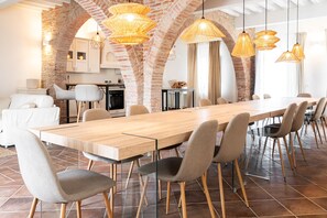 Een ruime eethoek met een lange houten tafel, meerdere stoelen en hangende rieten lampen.