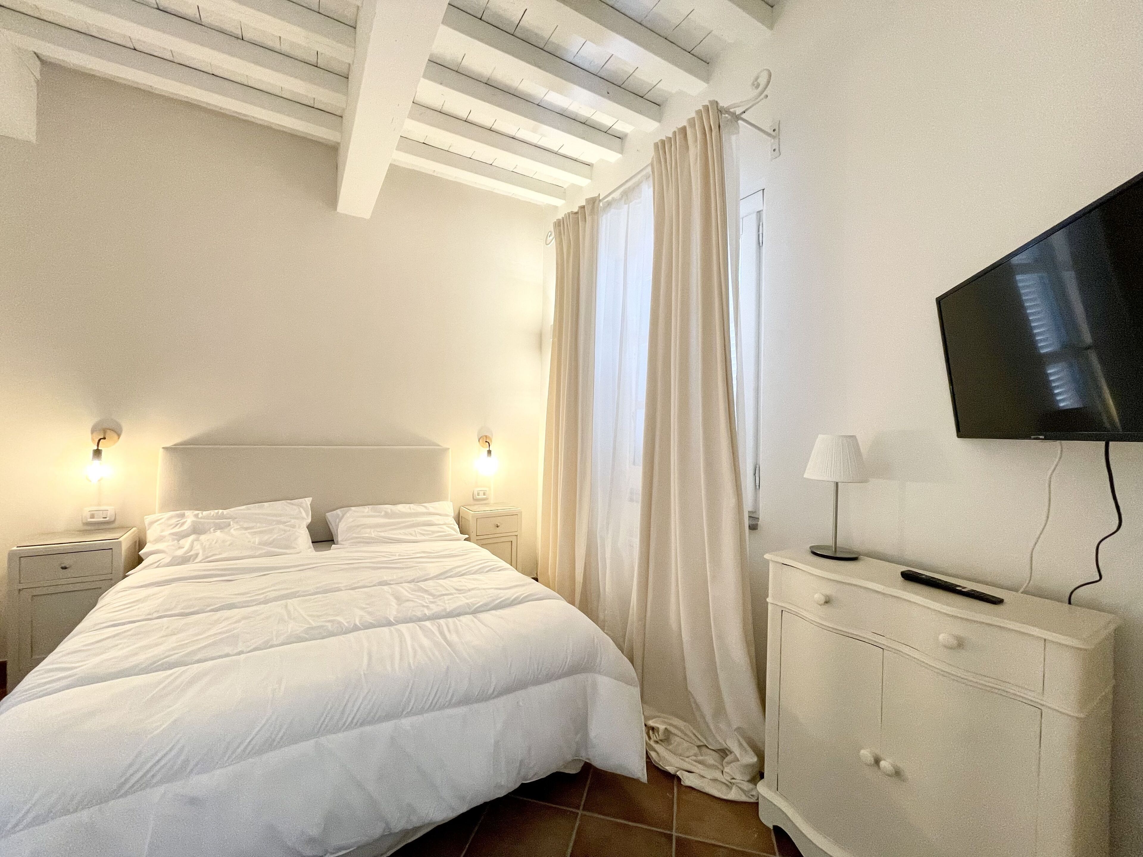 Una camera da letto con un letto, comodini, una TV e una cassettiera.