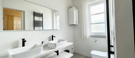 A modern bathroom with two sinks, a toilet, and a window.