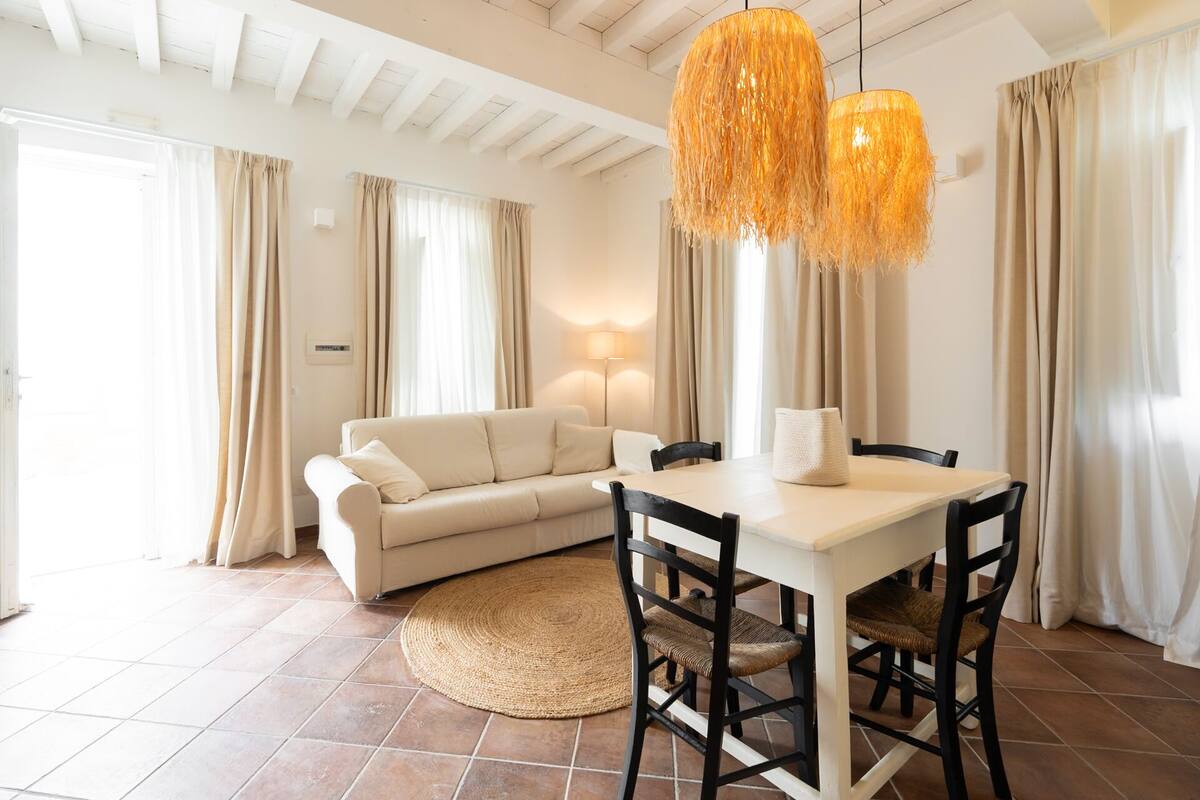 Una sala moderna con un sofá color beige, una mesa de comedor con sillas y una lámpara de araña grande de fibras naturales.