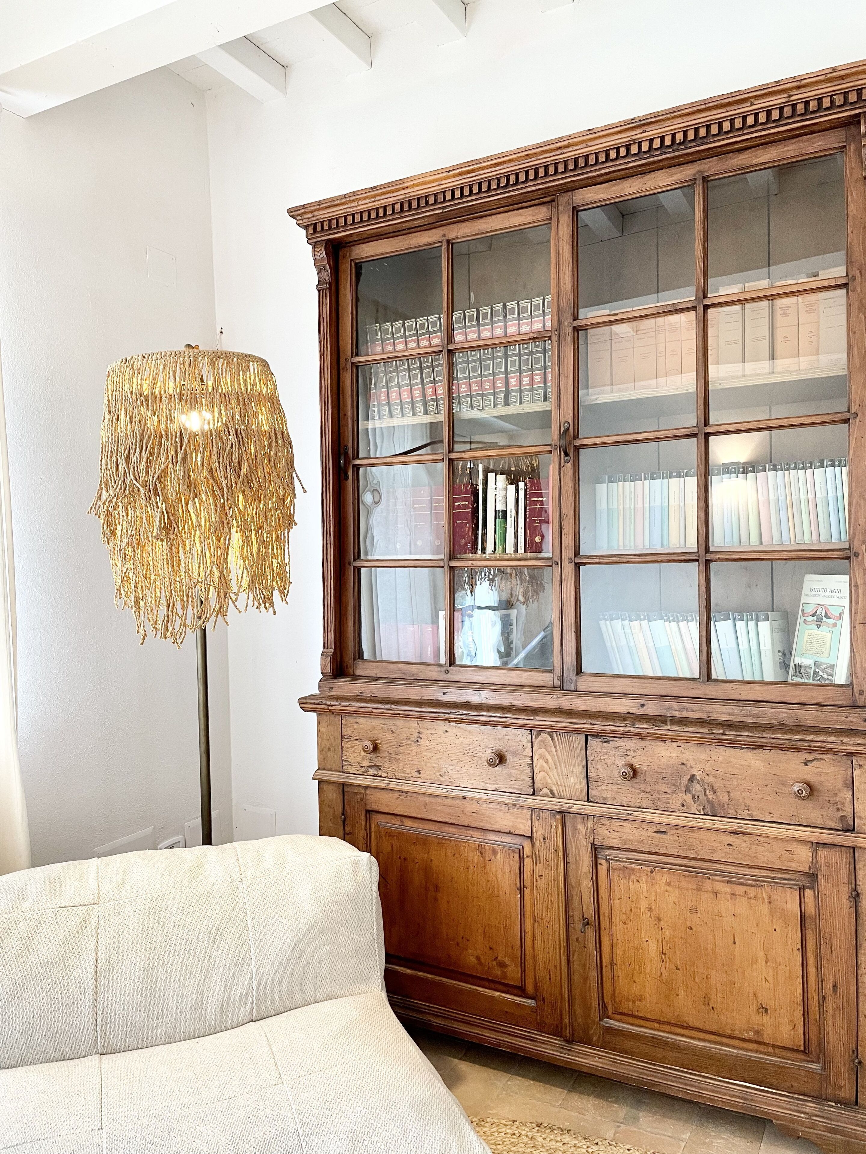 A room with a wooden cabinet containing books and decorative items, a textured lamp, and a white sofa.