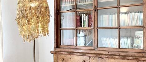 A room with a wooden cabinet containing books and decorative items, a textured lamp, and a white sofa.