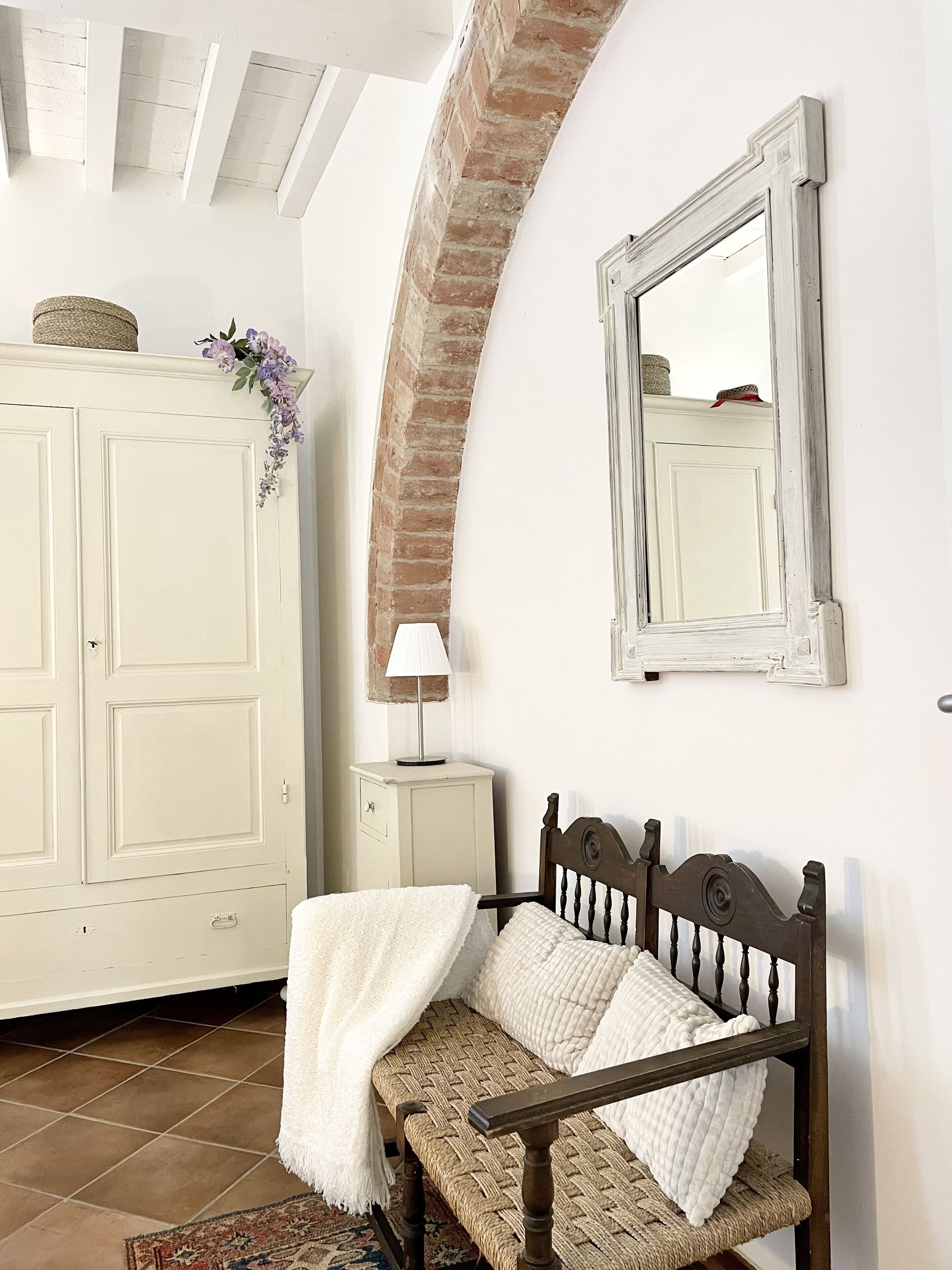 Una habitació amb una banca de fusta, un armari blanc, un mirall i una làmpada.