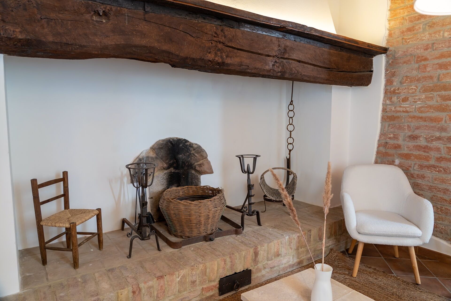Un interior rústico con chimenea de piedra, una silla blanca y una de madera.