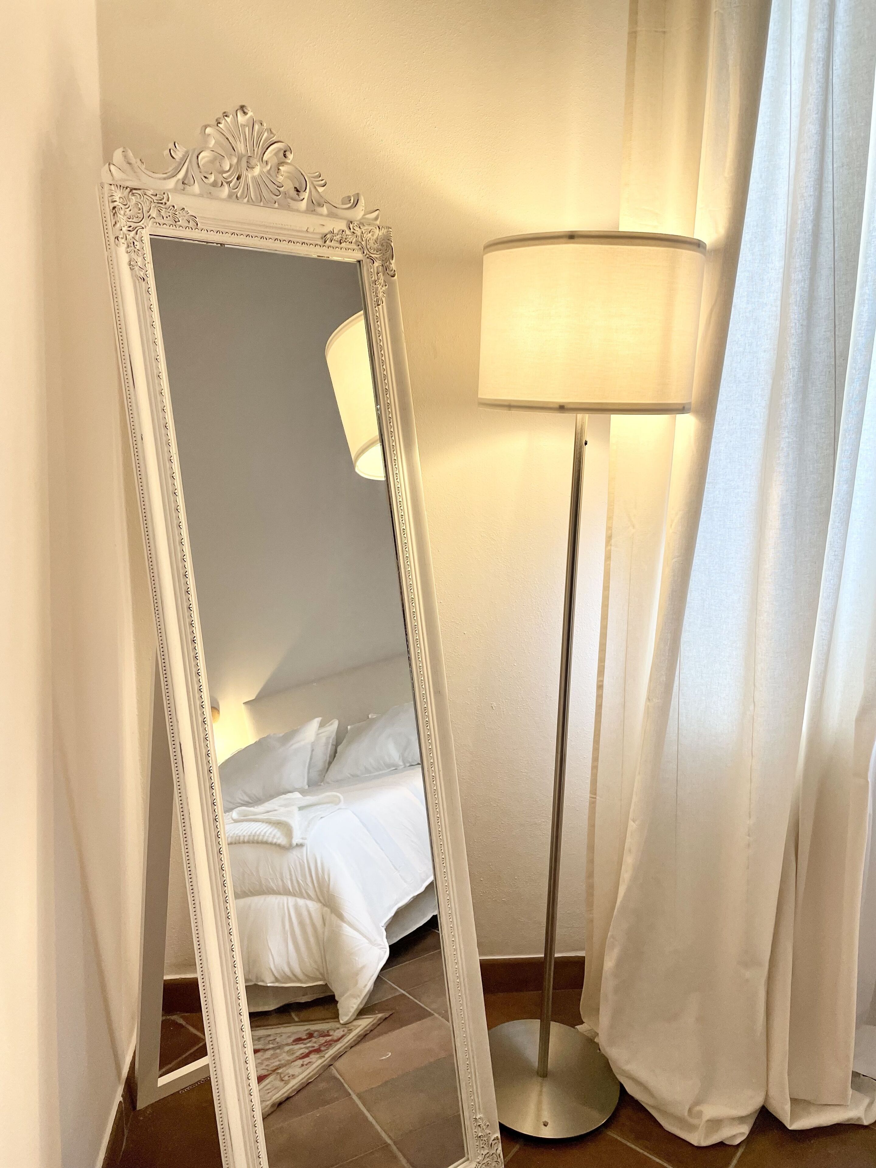 A bedroom with a bed, a floor lamp, and a mirror.
