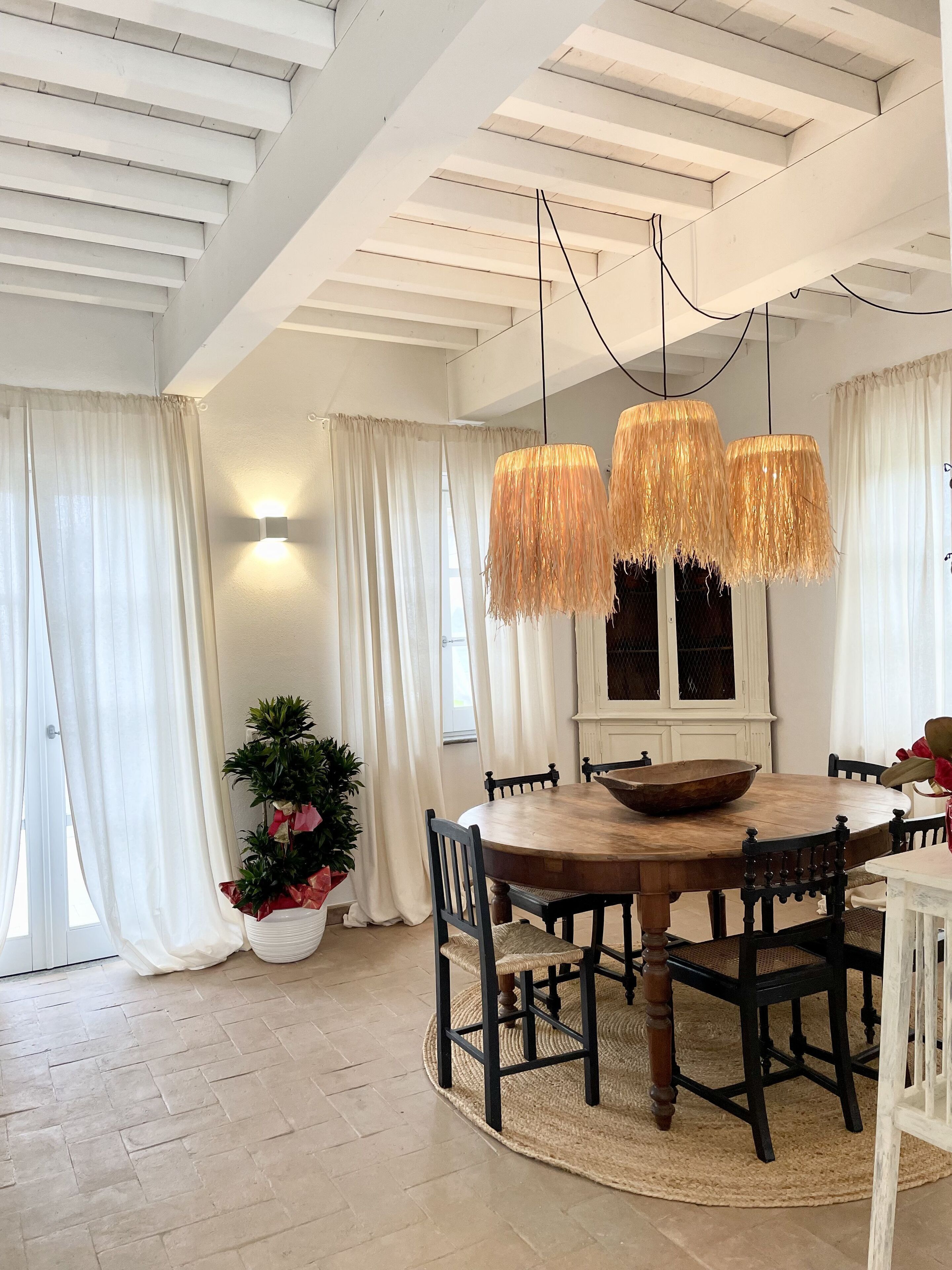 Un coin repas avec une table ronde en bois, des chaises noires, un tapis tissé et un luminaire suspendu.