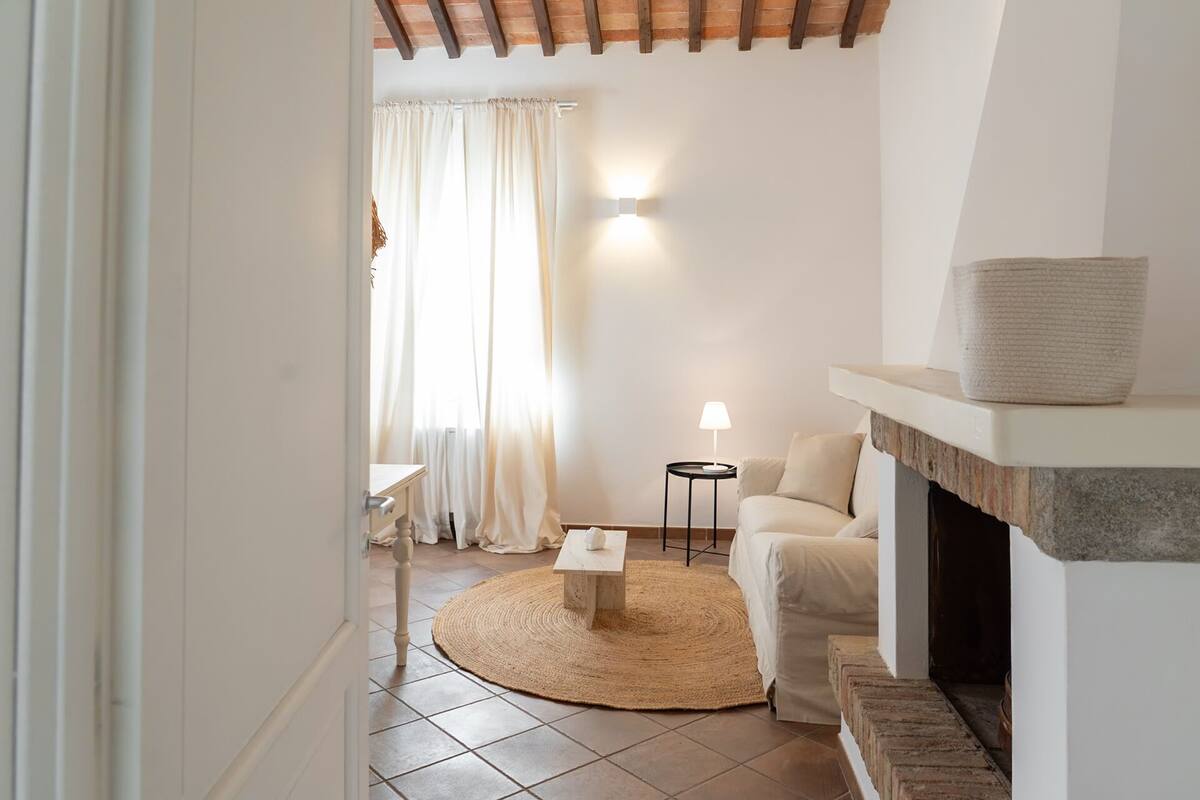 Una sala de estar acogedora con chimenea, un tapete redondo, un sofá y una mesita.