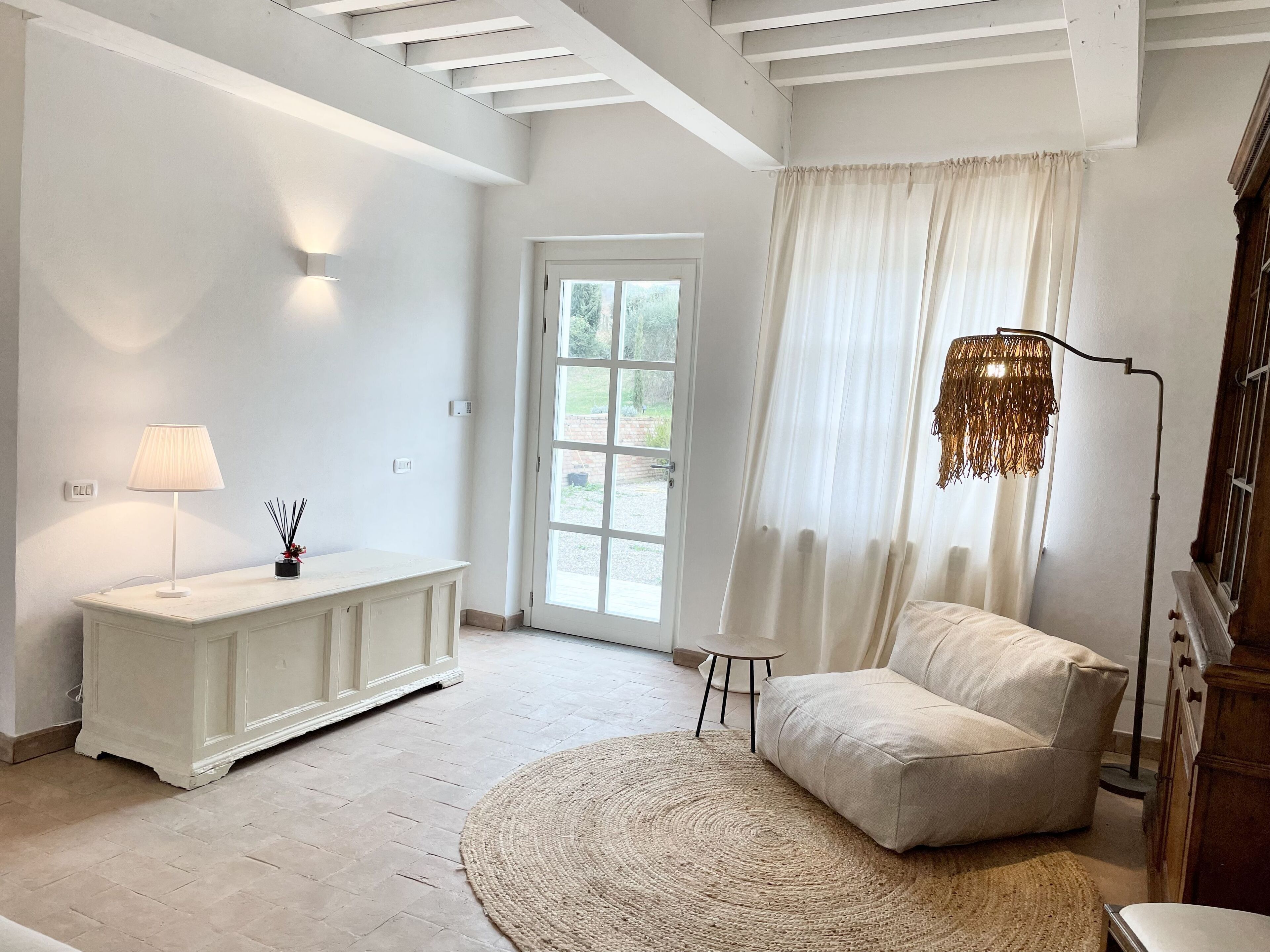 Een ruime kamer met een witte bank, een rond geweven vloerkleed, een witte console tafel met een lamp, en een vloerlamp.