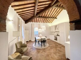 Un comedor con mesa y sillas, una cocina con armarios blancos y un techo abovedado con vigas a la vista.