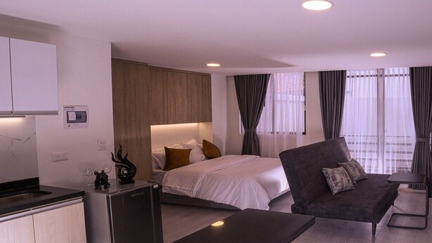Quarto de hotel moderno com uma cama, um sofá, uma pequena mesa e uma cozinha compacta.