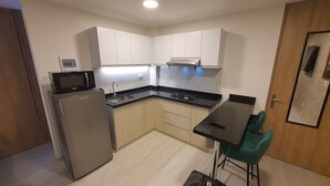 Cozinha compacta com geladeira, micro-ondas, fogão, pia e uma pequena mesa de jantar com duas cadeiras.