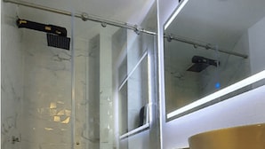 Casa de banho com chuveiro em cabine de vidro, sanita e espelho grande sobre a pia.