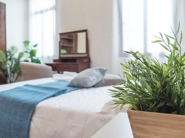 Ein Schlafzimmer mit einem Bett, einem Nachttisch, einem Spiegel und einer Zimmerpflanze.